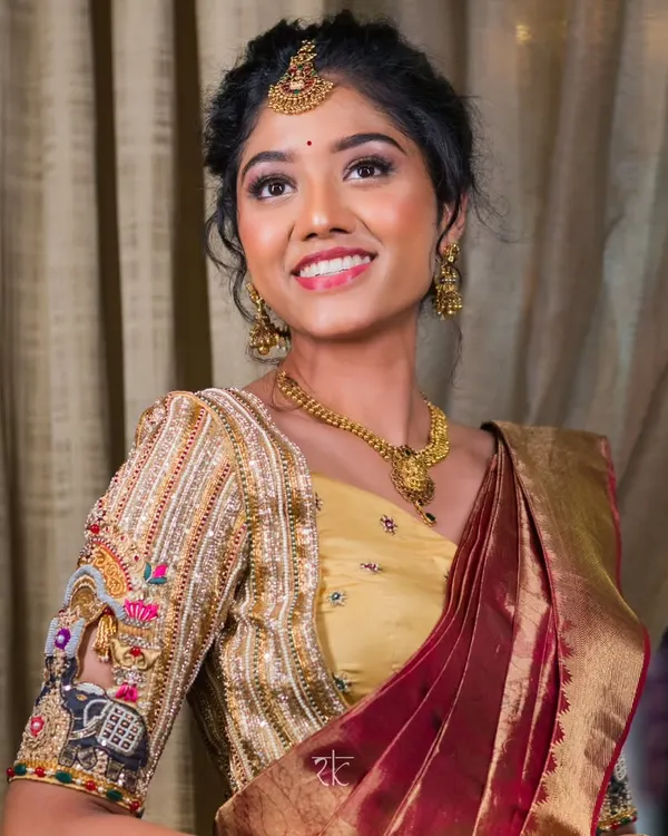 A smiling bride adorned in a masterpiece. This golden bridal blouse features incredibly detailed hand-embroidery, with motifs that tell a story, making her wedding day look truly one of a kind.