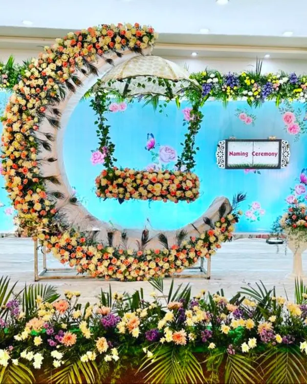 (Hero Item) A grand naming ceremony setup featuring a floral moon-shaped cradle swing. This design combines intricate flower arrangements with a unique structure to create a stunning centerpiece for your baby's special day.