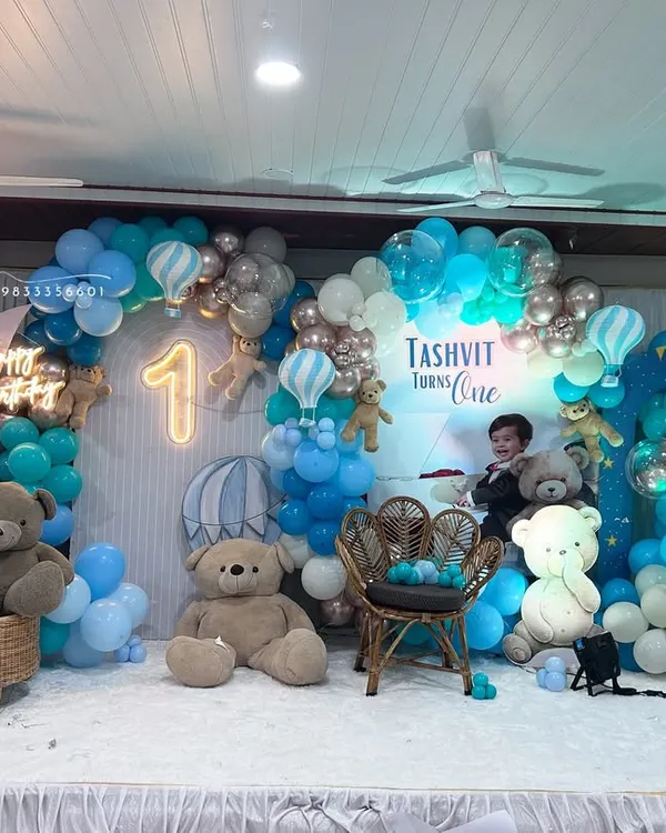We designed this grand teddy bear and hot air balloon theme for a first birthday party. This full-stage setup includes a custom backdrop, an extensive organic balloon arch in shades of blue and chrome, multiple teddy bear props, a peacock rattan chair for the birthday boy, and light-up marquee and neon numbers.