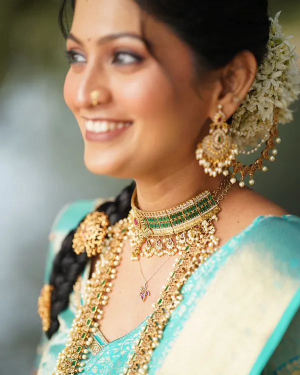 A beautiful close-up of a South Indian bridal look. This shot highlights the traditional braided hairstyle with gold accessories, the layered temple jewelry, and the soft, glowing makeup.