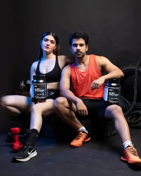 A powerful shot of male and female models posing with whey protein products in a stylized gym environment, perfect for brand campaigns and social media.