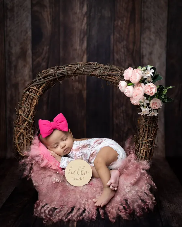 A perfect "Hello World" moment. This baby girl is sleeping peacefully in a rustic wreath basket, adorned with a bright pink bow and soft flowers.