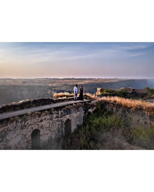 A cinematic drone shot of a couple during their pre-wedding session on an old stone bridge in Prayagraj. This high-angle view captures the vast landscape and the intimacy of the moment.