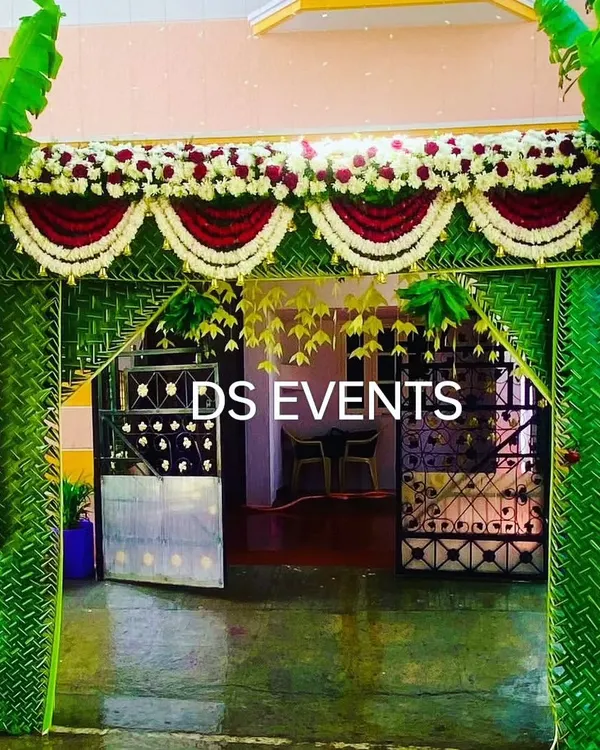 A traditional housewarming entrance arch. This design is built with a frame of woven coconut leaves, adorned with banana trees, and decorated with garlands of roses and jasmine for an auspicious welcome.