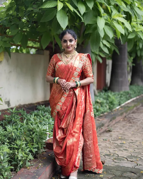 A full length view of a traditional red and gold Nauvari saree. This is a classic look for a Maharashtrian bride, complete with green bangles.