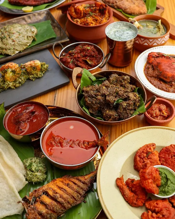 A lavish spread of authentic Konkani food, featuring fried fish, prawns, and various curries, styled to look like a generous family feast.