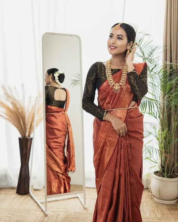 A professionally styled shot featuring a modern take on a traditional look. The makeup is clean and luminous, complementing the rich color of the saree and the contemporary setting.