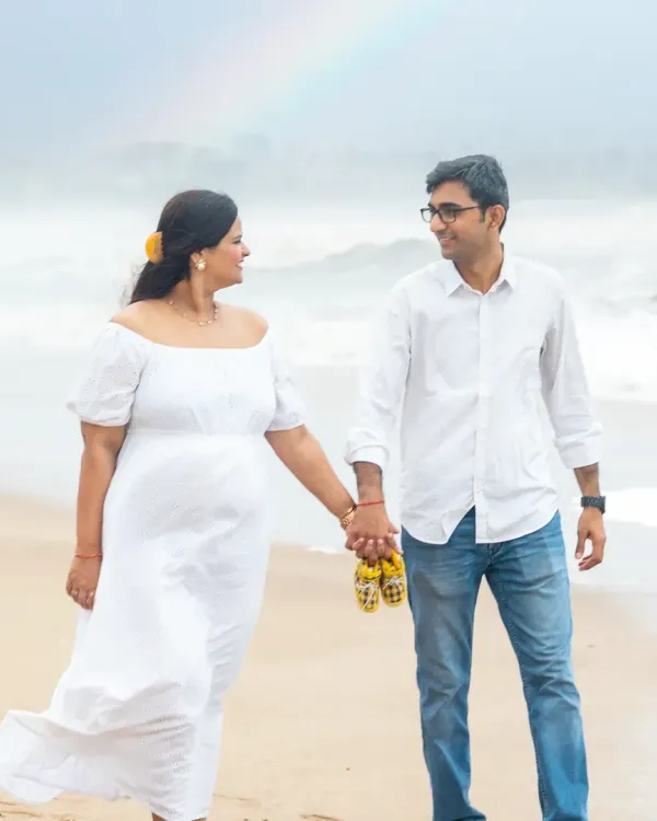A beautiful walk along the shore, with a rainbow gracing the sky. This couple is holding hands, carrying tiny baby shoes, stepping towards their future.