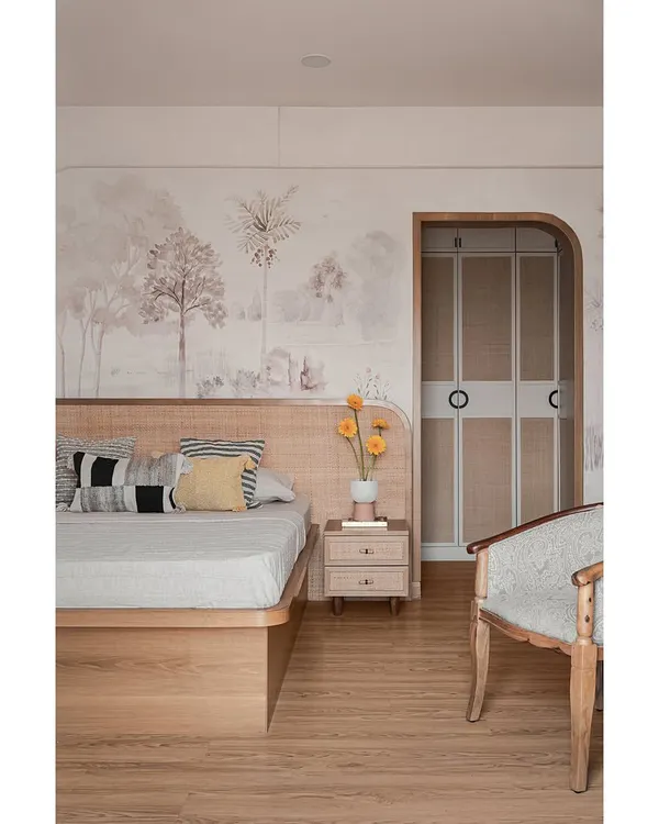 This master bedroom features a custom cane headboard set against a soft, tropical pastel wallpaper. An arched doorway with rounded cane-shutter doors leads to the walk-in wardrobe, adding a touch of warmth and modern minimalism.