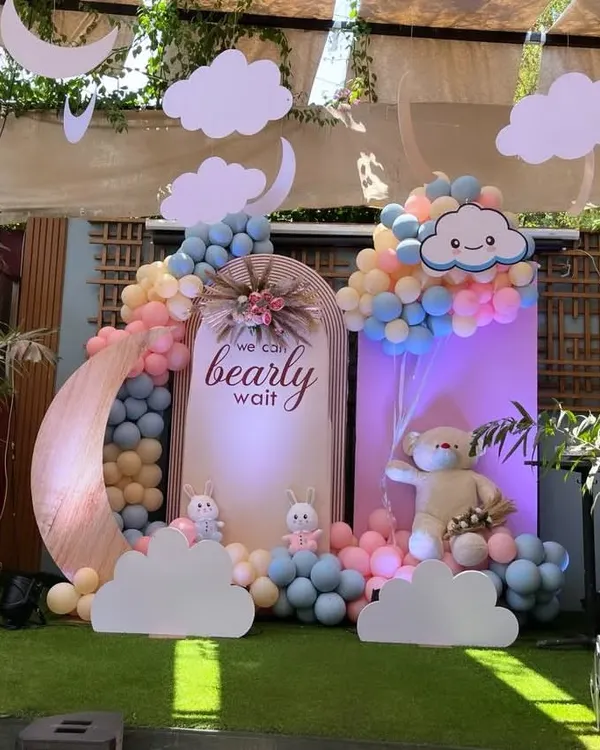 A dreamy "We Can Bearly Wait" baby shower theme. This outdoor setup features a pastel balloon arch, a large moon prop, and cute teddy bear and bunny figures.