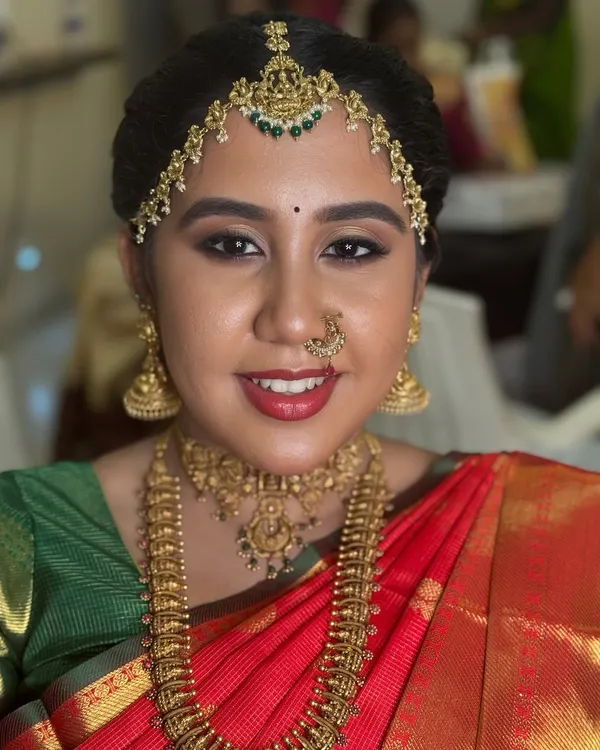 A classic South Indian Muhurtham look for my beautiful bride, Dr. Indhu. This look features a traditional red Kanjeevaram saree, complemented by radiant skin, bold red lips, and intricate gold temple jewellery, including a statement matha patti.