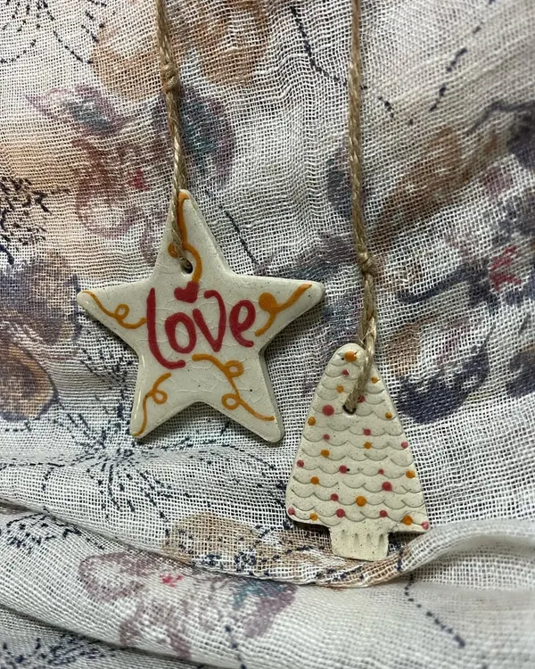 A set of 'All About Love' ornaments, featuring a star and a Christmas tree. The red and orange details are hand-painted, making each piece one-of-a-kind.
