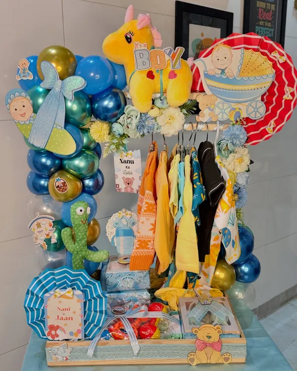 Our signature 'It's a Boy' baby wardrobe trousseau, fully assembled and ready to gift. It features a mini clothing rack with assorted outfits, a balloon arch, soft toys, and personalized cutouts, making it a stunning centerpiece for any baby shower or welcome party.