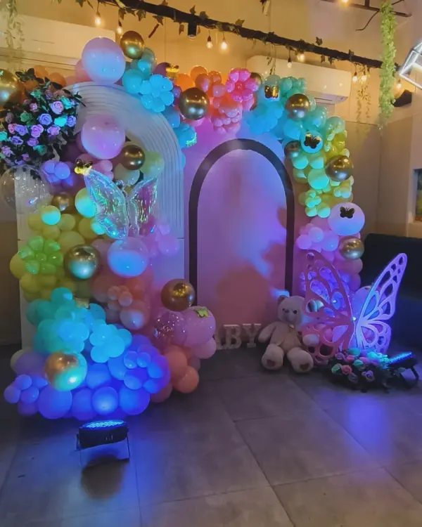 A magical, fairytale-themed decoration with rainbow lighting. This enchanting setup features glowing butterfly wings, a teddy bear, and a colorful balloon arch, creating a truly unique and dreamy atmosphere.