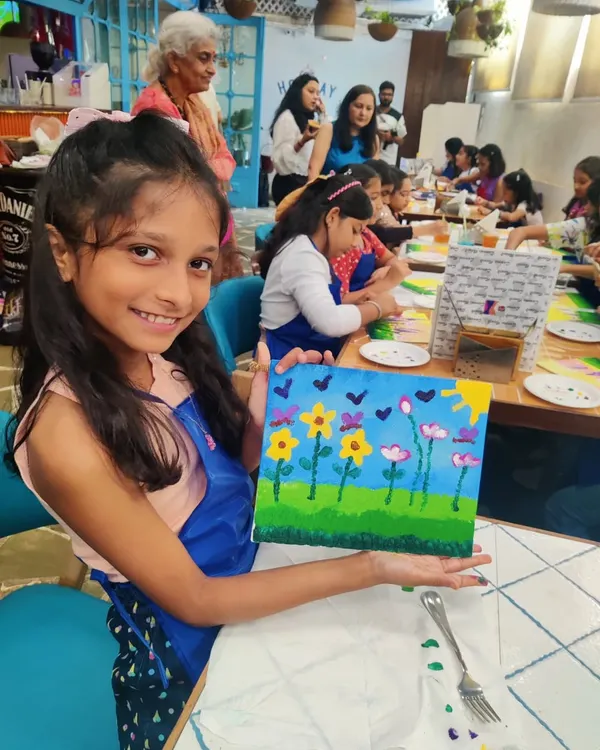 A young artist beaming with pride as she displays her finished floral canvas painting at Nishka's 10th birthday party.