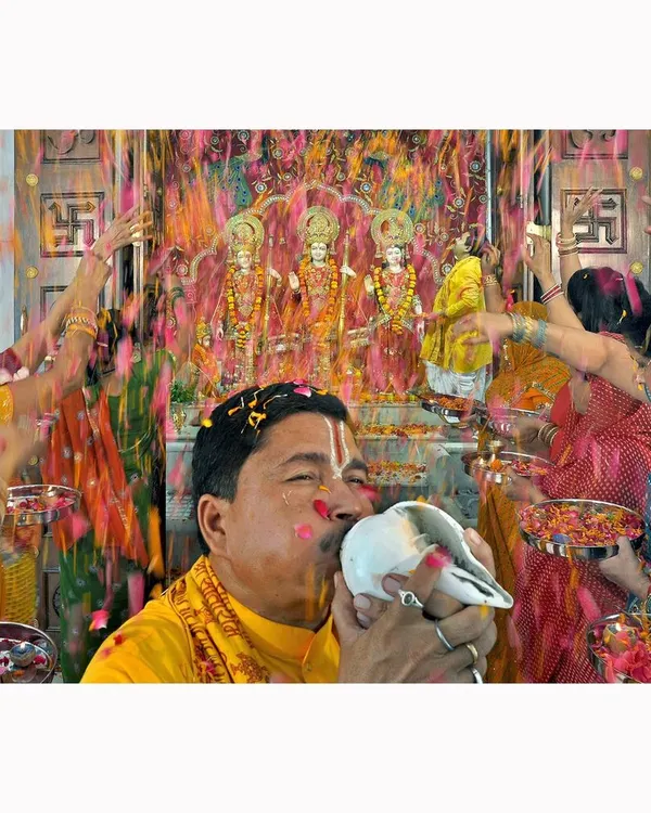A priest blows a conch shell during a temple ceremony, showered with flower petals. This image was part of a commissioned project and captures the sensory richness and devotion of the celebration.