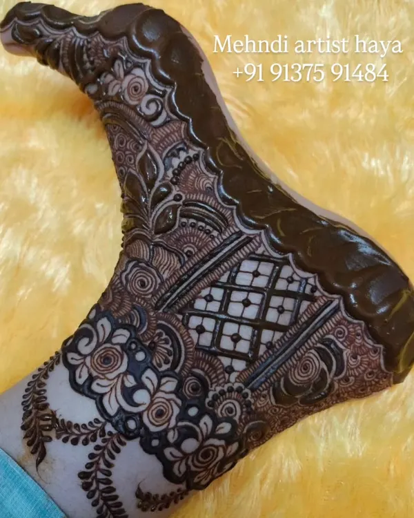 This is a full bridal foot design with the henna paste still on. The design features a combination of floral bands and a central grid pattern, covering the foot for a traditional look.