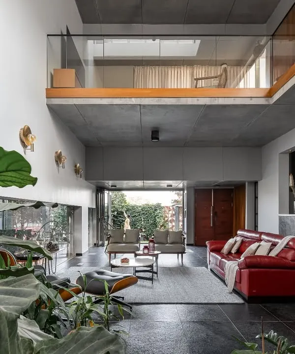 This is the heart of our project, 'Roots'. We designed this double-height living space to dissolve the boundaries between inside and out. The raw concrete ceiling and Cuddapah stone floor are balanced by the warmth of wood and the vibrant red sofa, creating a space that feels both expansive and inviting, with greenery flowing in from the garden.
