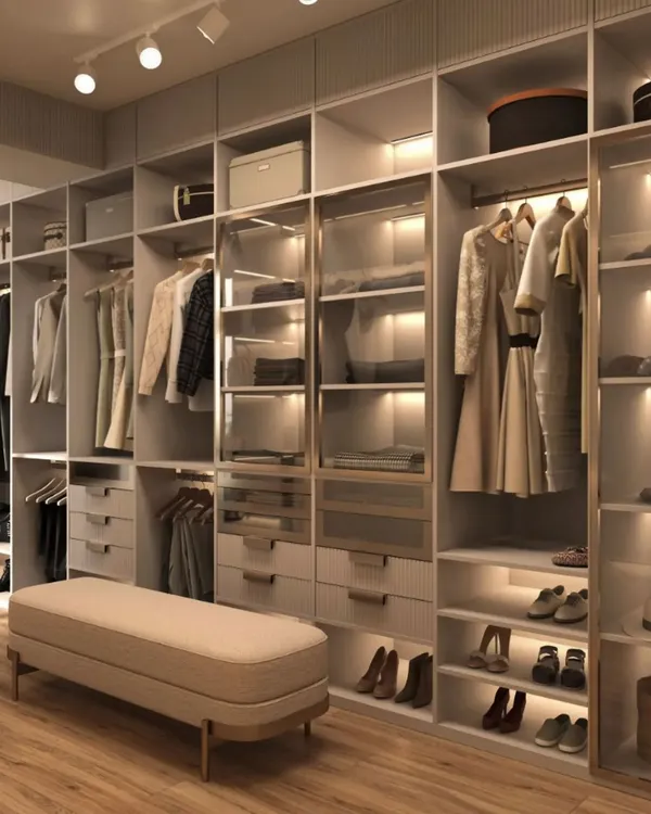 A spacious and well-organized walk-in closet with a neutral color palette. The design features a mix of hanging space, drawers, and open shelving with integrated lighting to illuminate clothing and accessories.