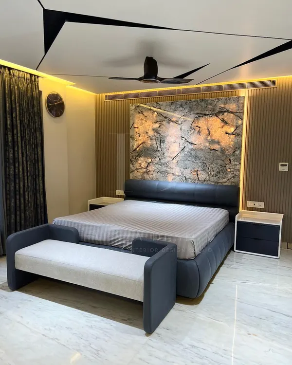 A complete view of a master bedroom I designed. It features a custom bed with a leather headboard, a matching bench, and sleek bedside tables, all set against a dramatic, back-lit marble-effect wall.