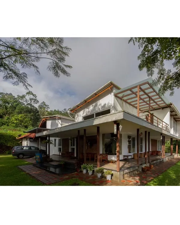 A wide-angle view of the 'Malenadu Mane', showing how the structure with its extended verandahs and sloping roofs sits comfortably within the green canopy of the surrounding coffee plantation.