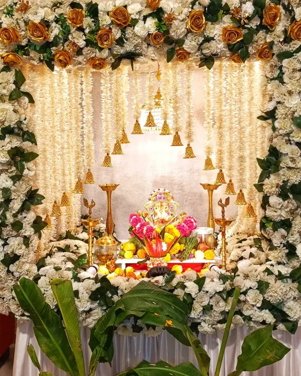 I created this classic Ganpati decoration for a home pooja. The setup features a dense frame of white and golden roses, a backdrop of delicate jasmine flower strings, and traditional brass bells and lamps to create a divine atmosphere for Bappa.