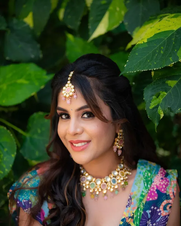 A perfect Mehendi portrait. The bride's happy smile, colorful jewelry, and the lush green background come together to create a fresh and joyful image.