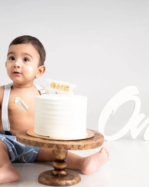The moment of anticipation just before the cake smash begins. This simple and clean first birthday setup captures the curiosity of a one-year-old with a classic white cake and suspenders.