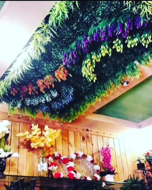 A full artificial garden panel installed directly onto the ceiling. This design uses a mix of hanging flowers and ferns to create a colorful, upside-down meadow effect.