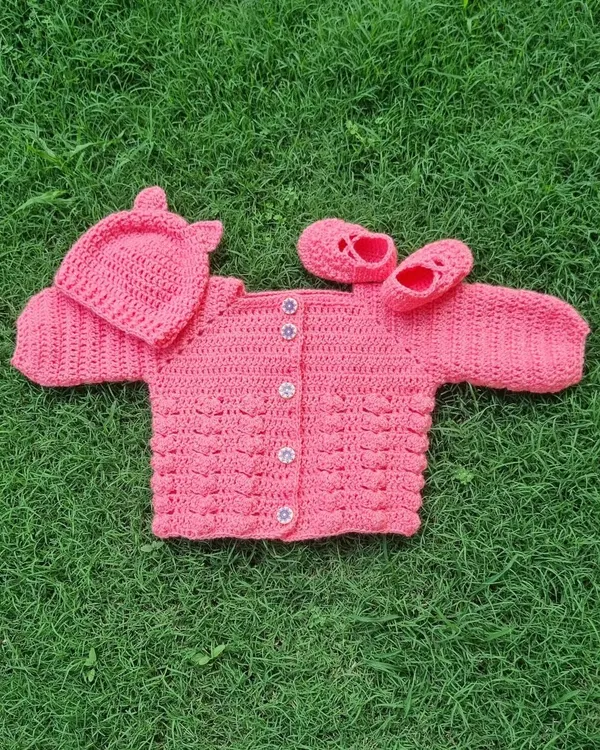 This adorable pink baby set includes a bobble-stitch sweater, a cute hat with little ears, and matching booties. It's crocheted with soft yarn, making it super comfortable for a little one.