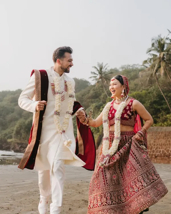 A candid shot of the couple laughing and running hand-in-hand on a Goa beach, perfectly capturing their joyful spirit in their wedding attire.