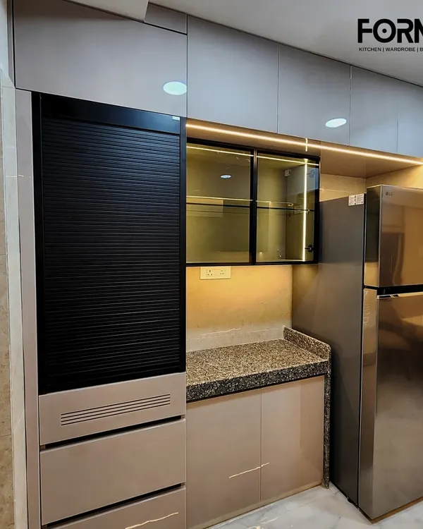 This view highlights the appliance garage with a roller shutter, seamlessly integrated next to the refrigerator. The combination of beige cabinets and granite countertops creates a warm and functional workspace.