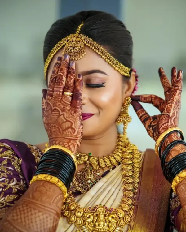 A beautiful bride adorned in a full antique gold temple jewellery set. The intricate details on the necklace, jhumkas, and maang tikka are perfectly highlighted in this shot, showing off her complete bridal radiance.