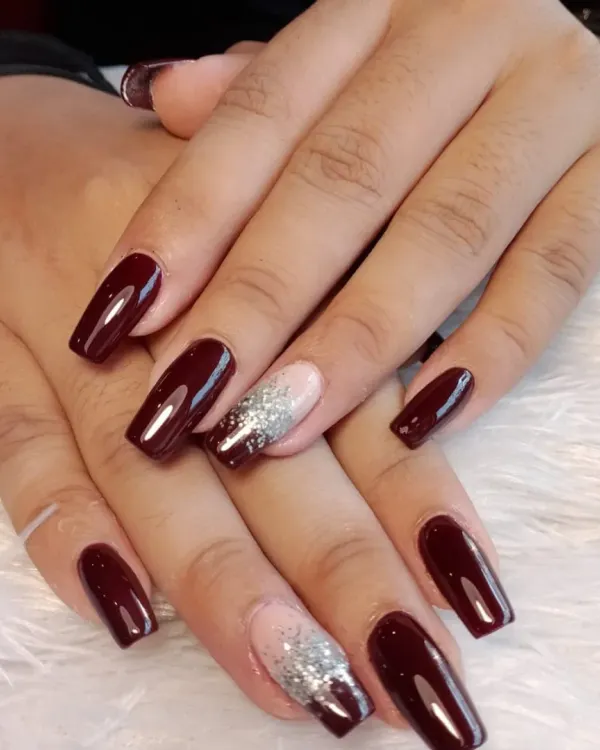 A rich, glossy burgundy polish on long, square-shaped nails. The look is elevated with two accent nails featuring a silver glitter gradient over a nude base, creating a perfect balance of bold color and sparkle.