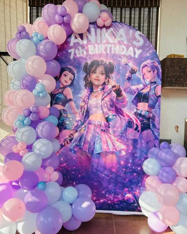 A cool and edgy 'Huntrix' themed backdrop for Anika's 7th birthday, surrounded by a pastel purple and blue balloon garland.