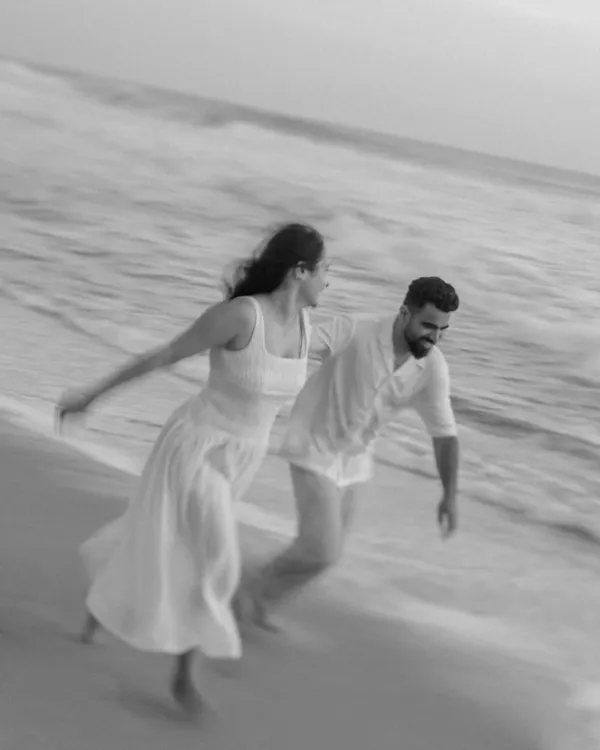 This black and white shot uses motion blur to capture the couple's joyful energy as they run along the shoreline. The lack of color emphasizes their movement and the timeless feeling of a carefree moment by the sea.