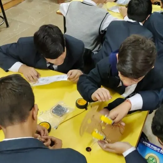 Students are deeply focused on assembling a robotic car kit during a workshop. This hands-on process teaches them about mechanics, motors, and chassis construction.