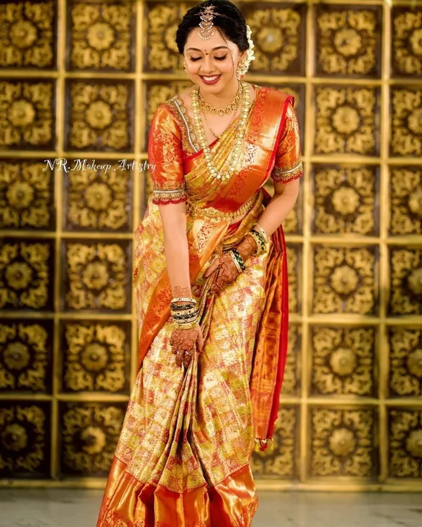 A full-length portrait of a radiant bride in her golden-hued wedding saree. The makeup is kept classic and luminous to complement the grandeur of her attire.