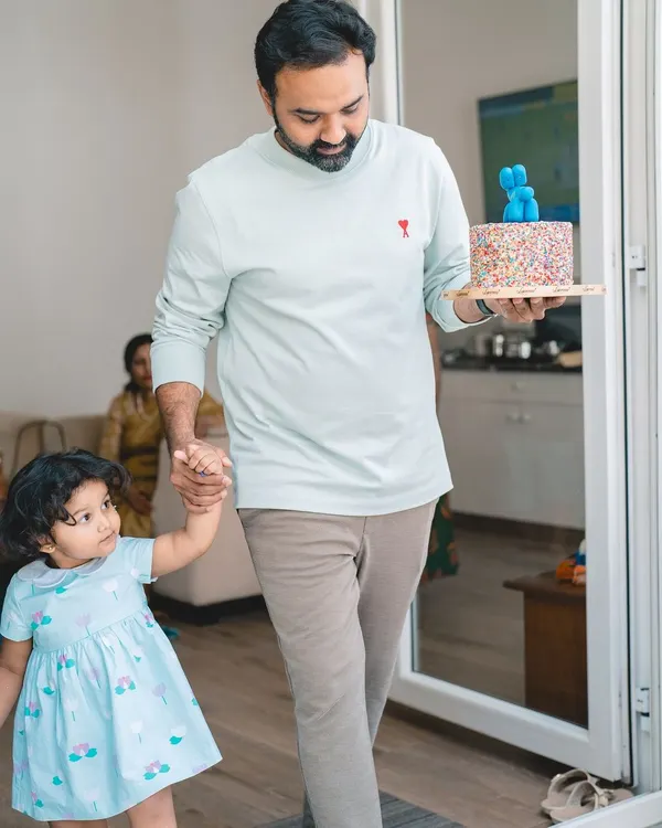 Here comes the cake! Capturing the anticipation of a birthday celebration, as a father proudly carries the cake while holding his daughter's hand.