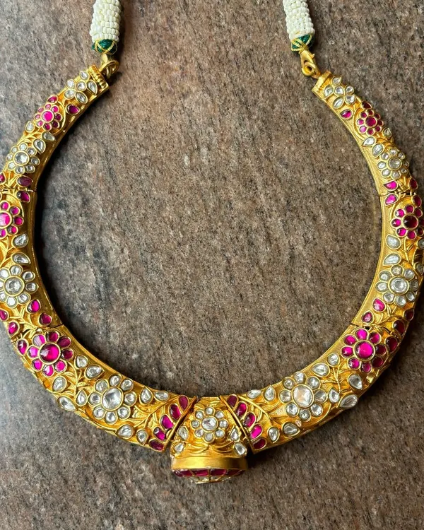 A unique and antique-style hasli necklace. This piece is crafted from silver with a gold-plated finish and is intricately adorned with pink and white Kundan stones for a rich, floral look.