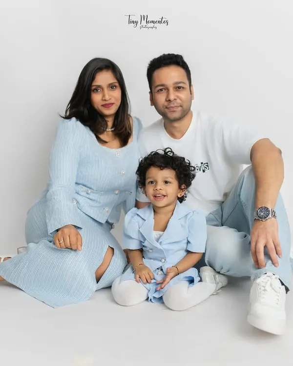 A classic family portrait with everyone looking towards the camera. The coordinated blue and white outfits create a serene and unified look against the minimalist white studio background.