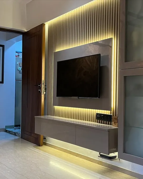 A full view of a modern TV wall unit. The combination of a fluted back panel, ambient lighting, and integrated storage creates a functional and visually appealing focal point in the living room.