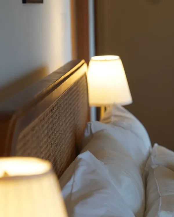 A detail of a rattan headboard glowing in the warm light of a bedside lamp, a moment of 'Rattan Grace'.