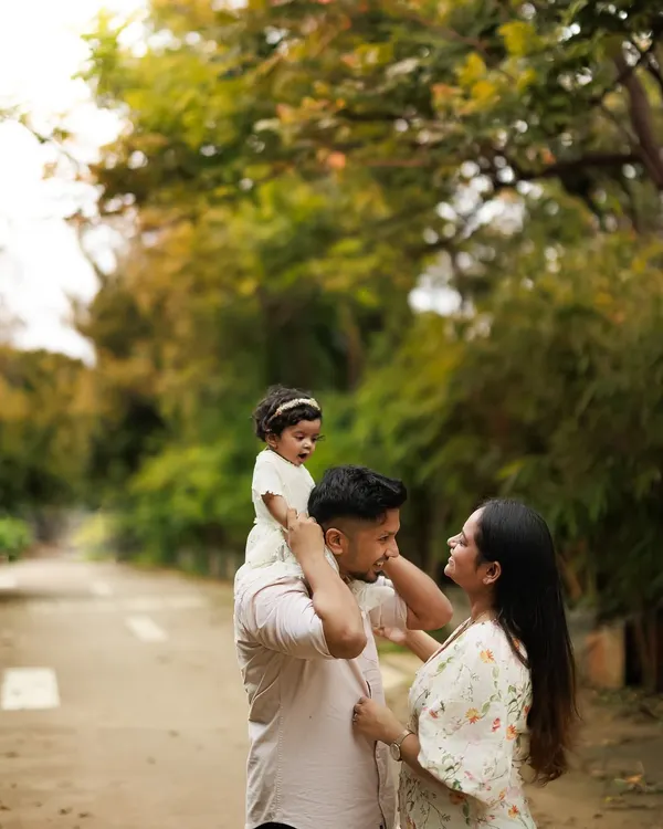 The partnership and joy in parenting shine through in this outdoor family portrait. A father carries his daughter on his shoulders while a mother looks on with love.