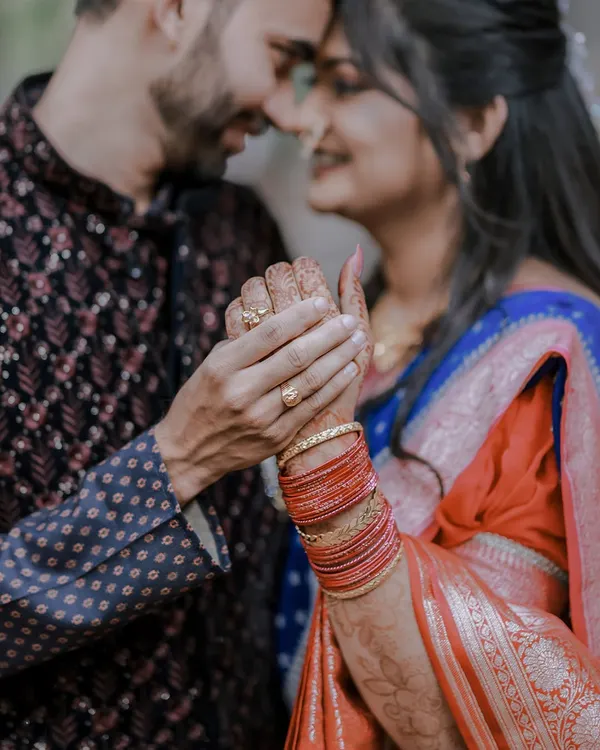 A close-up shot focusing on the couple's hands, showcasing the bride-to-be's intricate henna and colorful bangles. A beautiful detail from a Maharashtrian engagement.