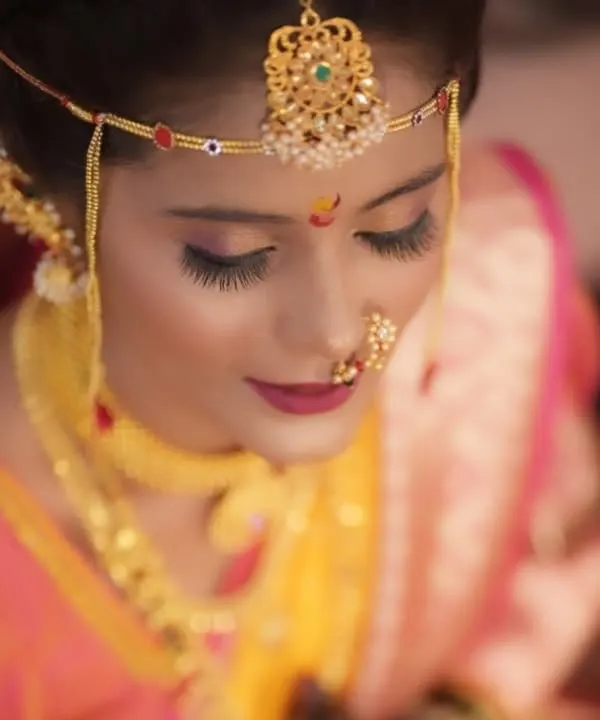 A detailed close-up of a Maharashtrian bride, focusing on the traditional 'mundavalya' (forehead ornament), expressive eye makeup, and a classic nath.