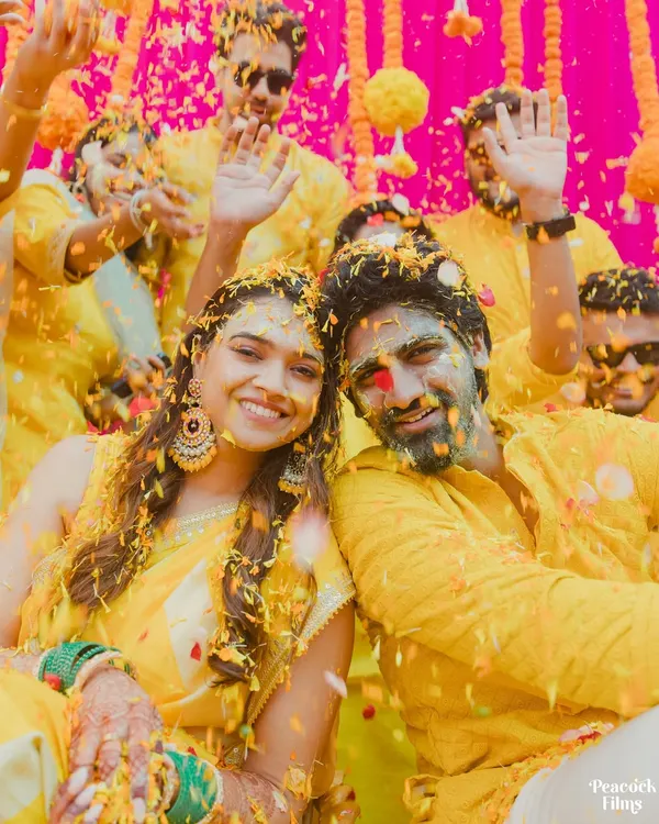 A Haldi ceremony that's a true explosion of joy! This shot captures the couple and their friends mid-celebration, covered in turmeric and flower petals, with pure happiness on their faces.