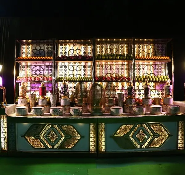An elaborate and beautifully illuminated buffet counter for a grand wedding. The intricate latticework and multi-level shelving create a stunning display for a wide variety of beverages and dishes.