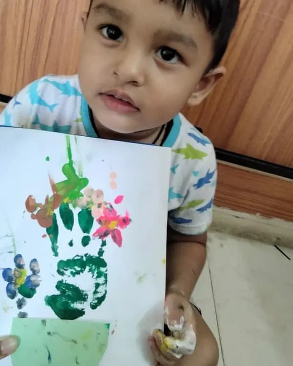 A happy student showing off his handprint flower pot painting. Art and craft activities like this are not just for fun; they help develop fine motor skills, color recognition, and a child's creative expression.