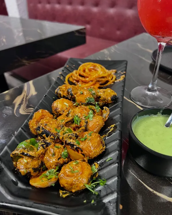 A beautifully plated dish of tandoori mushrooms. The dark plate makes the colors of the dish and the green chutney pop, and the overhead angle shows off the presentation.
